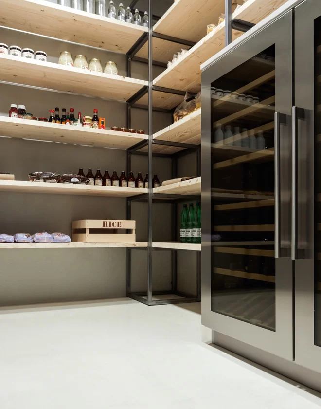 Materika walk-in pantry featuring open wood shelving, technical metal frames, and integrated stainless steel wine coolers.