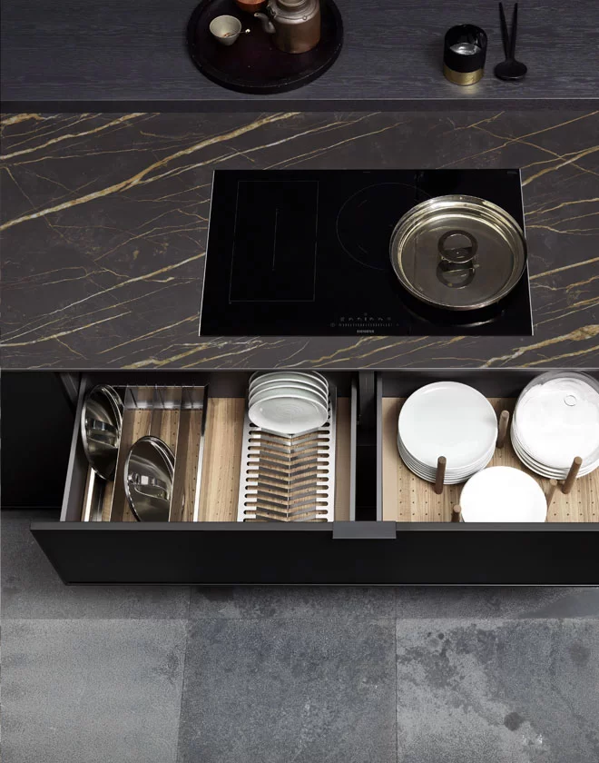 Luxury Quadra kitchen island featuring a black marble-effect countertop with an induction cooktop and bespoke internal dish organizers in a deep-toned drawer.